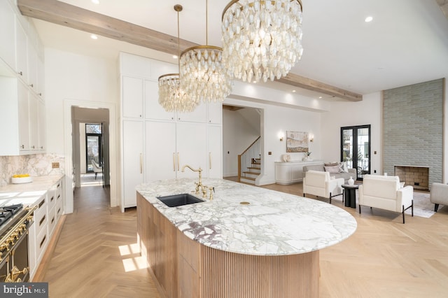 kitchen featuring beamed ceiling, a sink, open floor plan, an inviting chandelier, and a fireplace