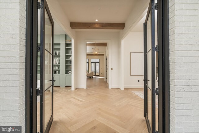 hallway featuring beamed ceiling, brick wall, and baseboards