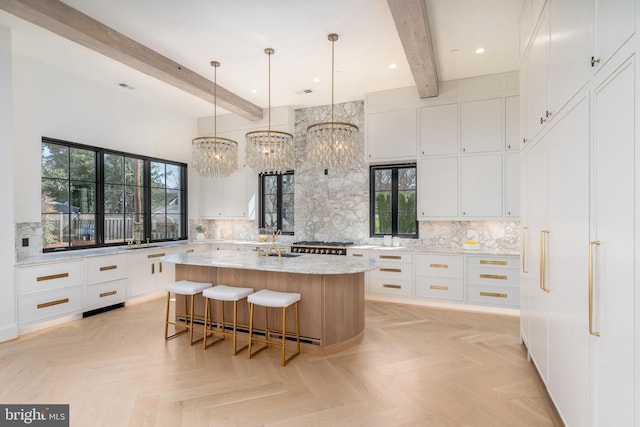 kitchen with beam ceiling, tasteful backsplash, a kitchen island with sink, and white cabinets