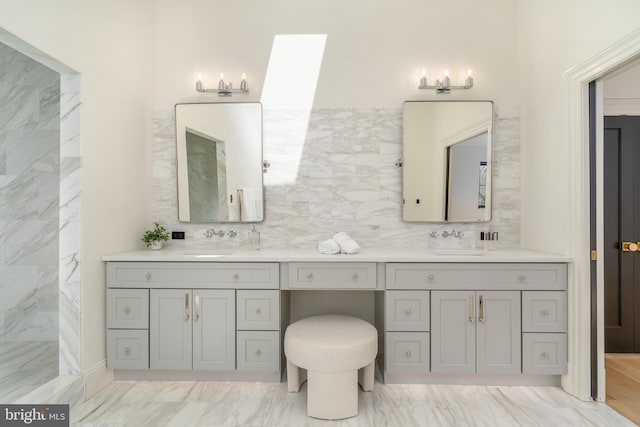 bathroom featuring a sink, marble finish floor, a skylight, and double vanity