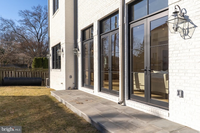 doorway to property with brick siding, a lawn, french doors, and fence