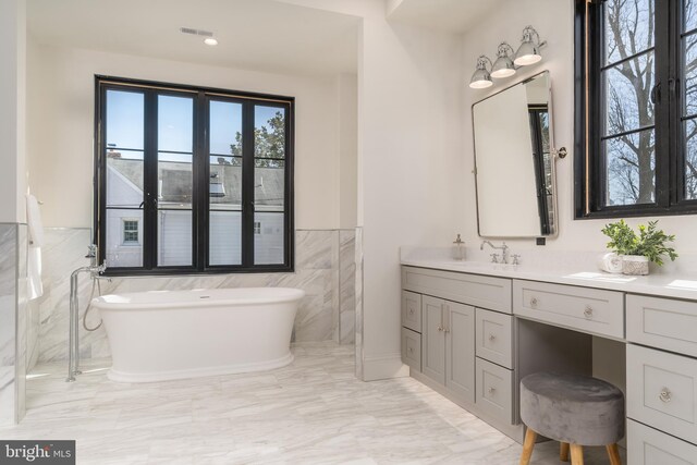 full bath featuring visible vents, tile walls, wainscoting, a soaking tub, and vanity