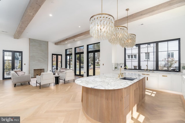 kitchen with beam ceiling, a sink, light stone counters, a towering ceiling, and a chandelier