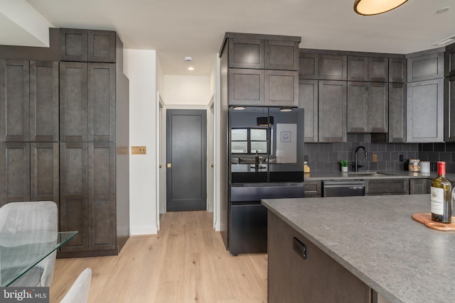 kitchen with tasteful backsplash, dark brown cabinetry, light wood-type flooring, refrigerator with glass door, and a sink