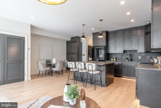 kitchen featuring tasteful backsplash, dishwasher, light wood-type flooring, refrigerator, and a sink