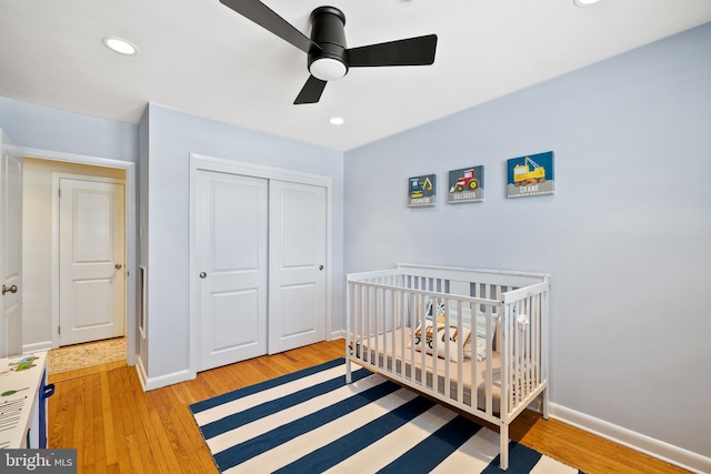 bedroom with ceiling fan, a closet, a crib, and wood-type flooring