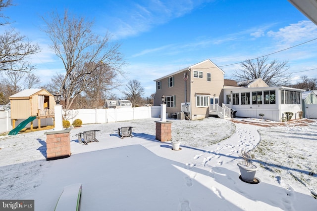 yard covered in snow featuring a fire pit, a playground, and a sunroom