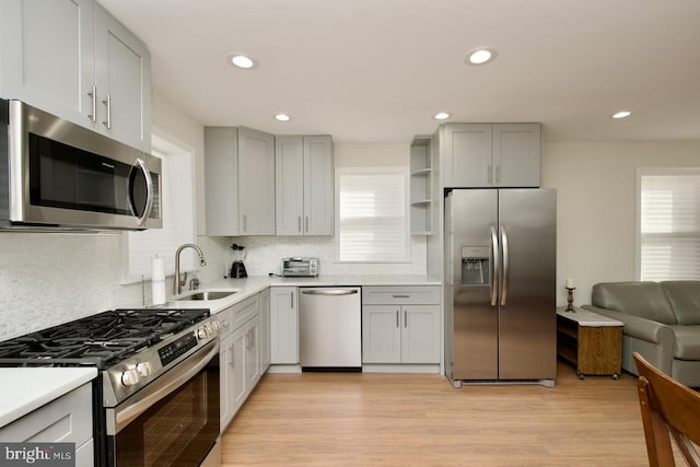 kitchen with sink, light hardwood / wood-style flooring, gray cabinets, appliances with stainless steel finishes, and decorative backsplash