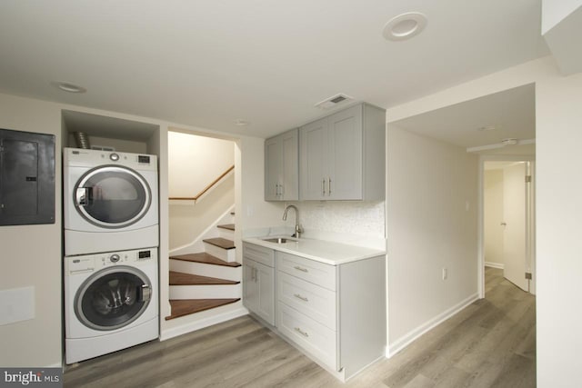 washroom with stacked washer / dryer, electric panel, sink, and light hardwood / wood-style flooring