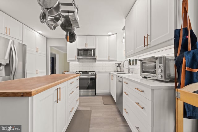 kitchen with sink, white cabinetry, tasteful backsplash, appliances with stainless steel finishes, and light hardwood / wood-style floors