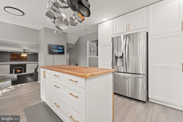 kitchen featuring a stone fireplace, wood counters, white cabinetry, ceiling fan, and stainless steel refrigerator with ice dispenser