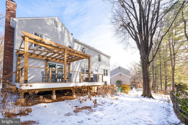 snow covered back of property with a deck and a pergola