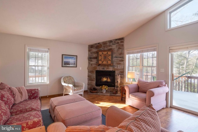 living room featuring light hardwood / wood-style flooring, a stone fireplace, lofted ceiling, and plenty of natural light