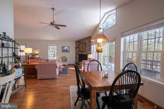 dining area with lofted ceiling, wood-type flooring, ceiling fan, and a stone fireplace