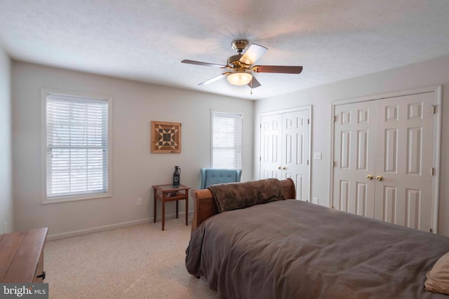 carpeted bedroom featuring ceiling fan, multiple closets, multiple windows, and a textured ceiling