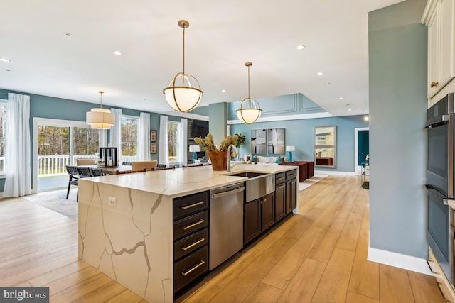 kitchen with light stone countertops, pendant lighting, a center island with sink, appliances with stainless steel finishes, and sink