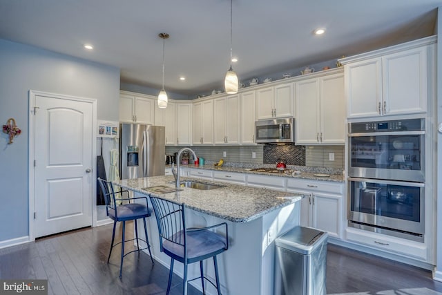 kitchen with stainless steel appliances, sink, decorative light fixtures, white cabinets, and a kitchen island with sink