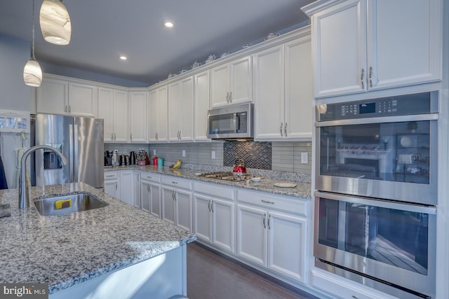 kitchen featuring appliances with stainless steel finishes, light stone countertops, sink, white cabinetry, and decorative light fixtures