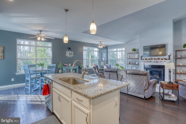 kitchen with sink, decorative light fixtures, dishwasher, light stone counters, and an island with sink