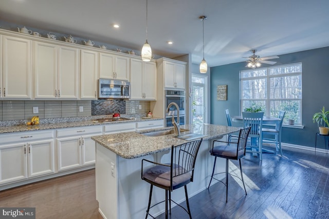 kitchen featuring stainless steel appliances, sink, ceiling fan, an island with sink, and hanging light fixtures