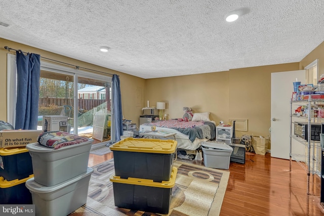 bedroom featuring wood-type flooring, access to exterior, and a textured ceiling