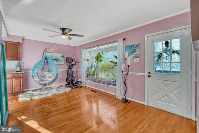 foyer entrance featuring ornamental molding, light wood-type flooring, ceiling fan, and a healthy amount of sunlight