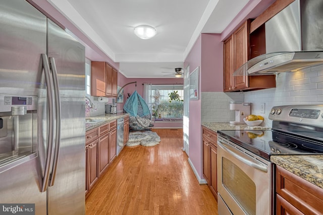 kitchen with appliances with stainless steel finishes, wall chimney range hood, and light stone countertops