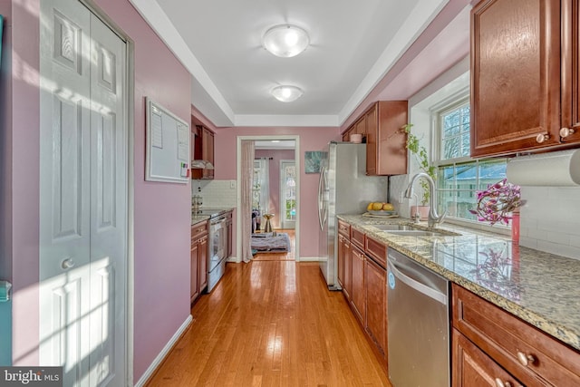 kitchen with light stone counters, light hardwood / wood-style flooring, stainless steel appliances, tasteful backsplash, and sink