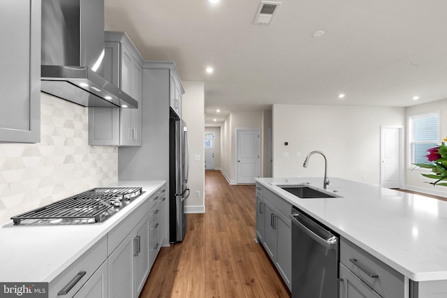 kitchen with stainless steel appliances, wall chimney range hood, backsplash, gray cabinetry, and sink