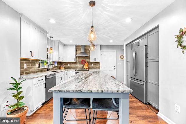 kitchen with a center island, decorative light fixtures, stainless steel appliances, wall chimney range hood, and a kitchen breakfast bar