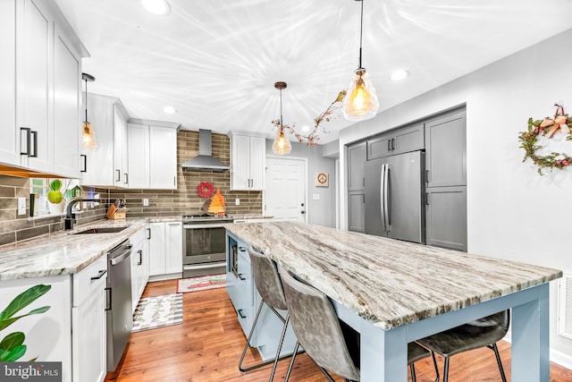 kitchen with wall chimney exhaust hood, hanging light fixtures, appliances with stainless steel finishes, a kitchen breakfast bar, and sink