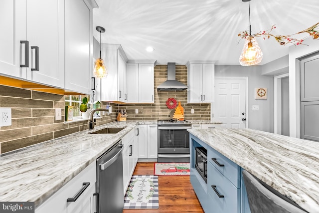 kitchen featuring stainless steel appliances, sink, white cabinetry, wall chimney range hood, and decorative light fixtures