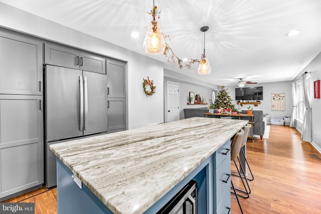 kitchen with decorative light fixtures, a center island, a kitchen breakfast bar, built in refrigerator, and ceiling fan