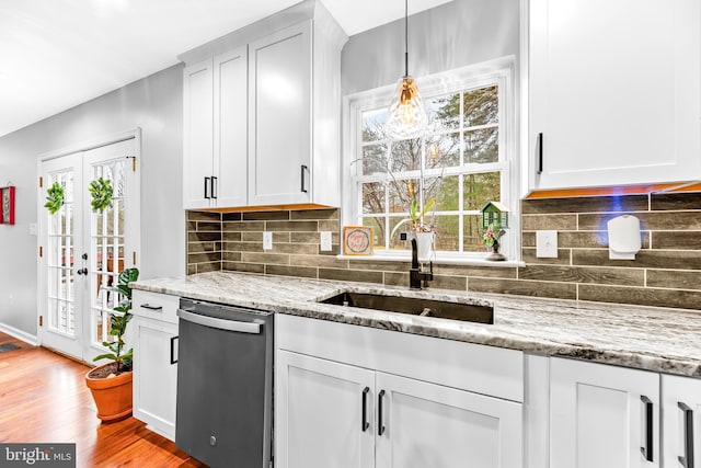 kitchen featuring decorative light fixtures, white cabinetry, light hardwood / wood-style flooring, stainless steel dishwasher, and light stone countertops