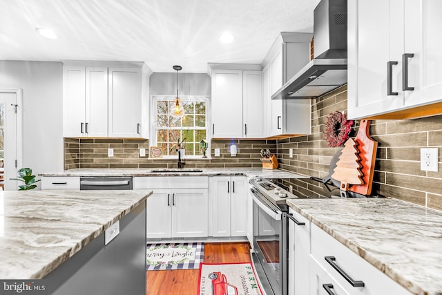 kitchen featuring hardwood / wood-style flooring, hanging light fixtures, wall chimney range hood, appliances with stainless steel finishes, and sink