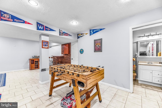 recreation room with a textured ceiling, light tile patterned flooring, and sink