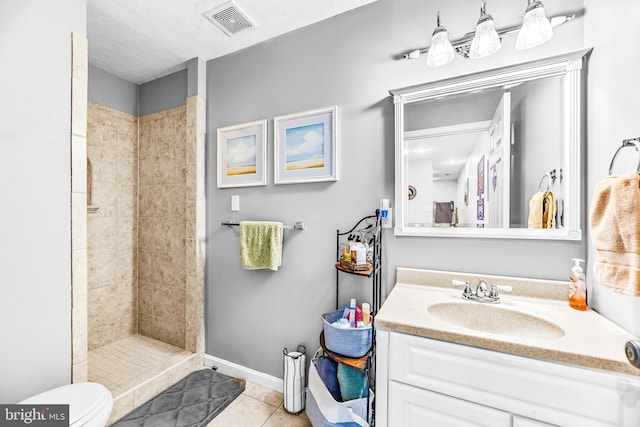 bathroom with toilet, tile patterned flooring, vanity, and tiled shower