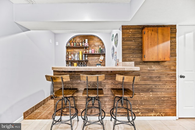 bar with wooden walls, built in features, and light tile patterned floors