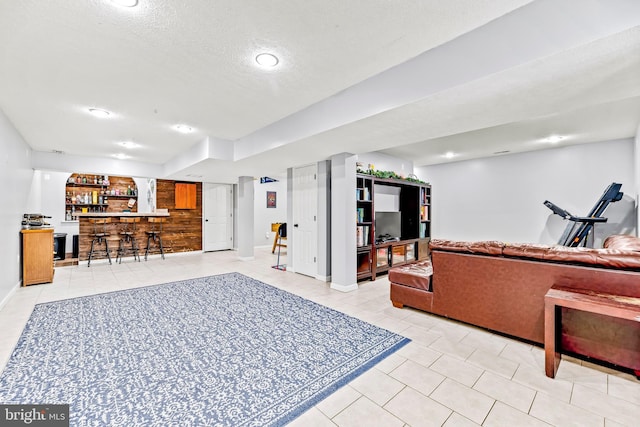 living room featuring light tile patterned floors, a textured ceiling, and bar area