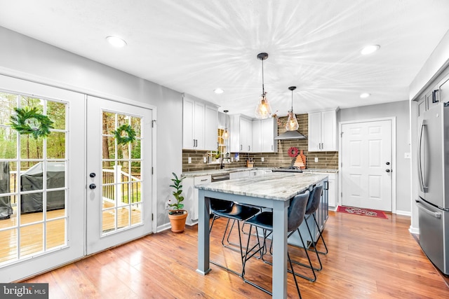 kitchen featuring wall chimney exhaust hood, hanging light fixtures, a center island, stainless steel refrigerator, and white cabinets