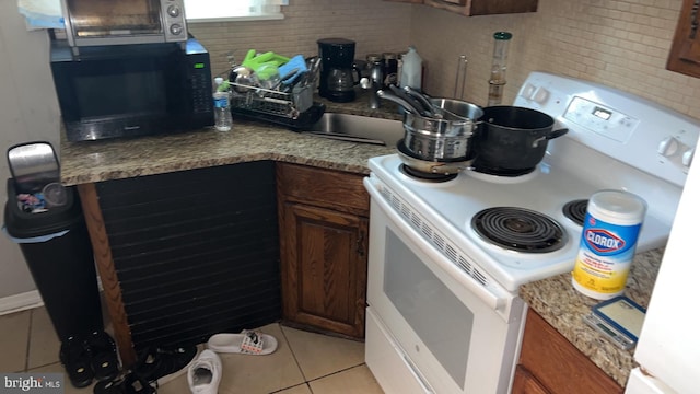 kitchen with white electric range oven, light tile patterned floors, tasteful backsplash, and sink