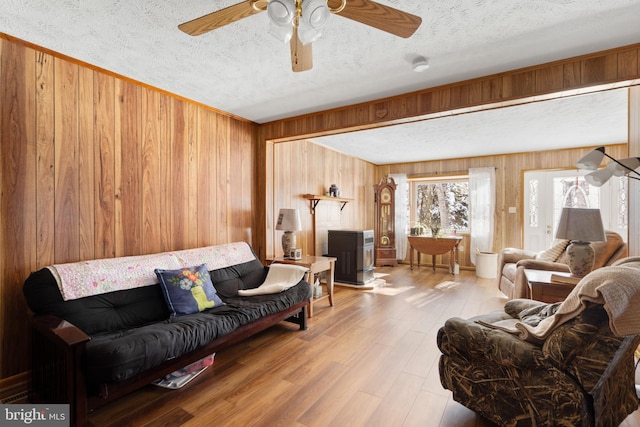 living room featuring a textured ceiling, ceiling fan, light hardwood / wood-style flooring, and wood walls