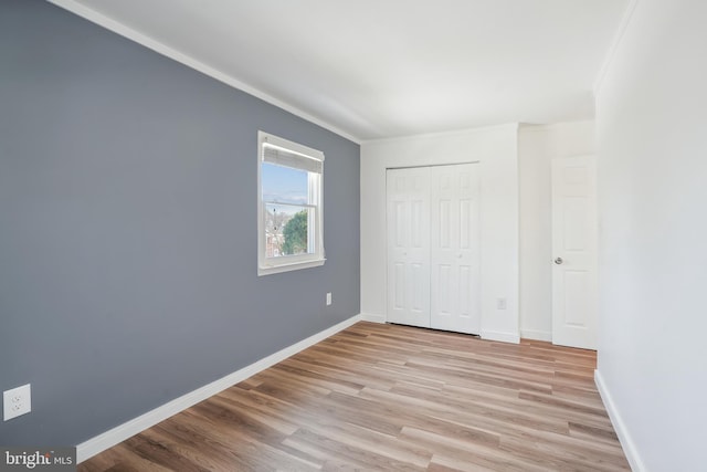 unfurnished bedroom featuring a closet, crown molding, and light wood-type flooring