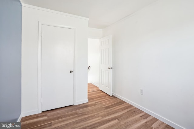 unfurnished bedroom featuring wood-type flooring, a closet, and ornamental molding