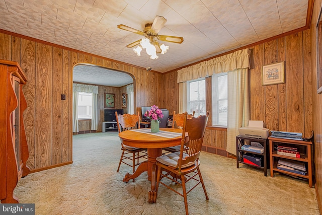 dining area with ornamental molding, a wealth of natural light, light colored carpet, and wood walls