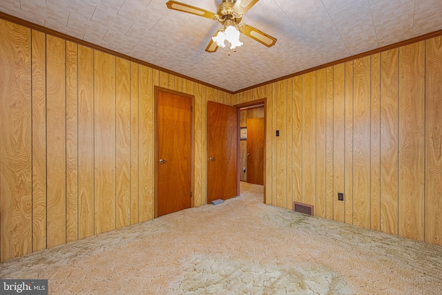 carpeted spare room featuring wooden walls and ceiling fan