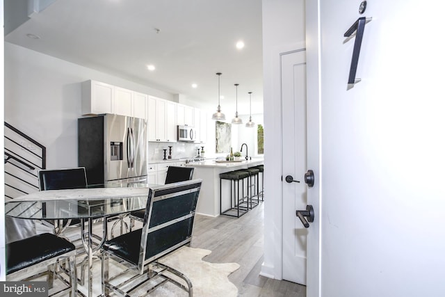 kitchen with white cabinetry, stainless steel appliances, light wood-type flooring, a kitchen breakfast bar, and hanging light fixtures