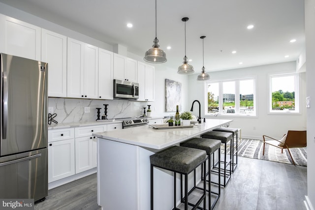 kitchen featuring decorative light fixtures, a center island with sink, white cabinetry, appliances with stainless steel finishes, and light stone counters