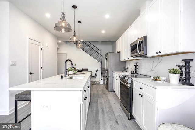 kitchen featuring decorative light fixtures, sink, white cabinetry, a kitchen island with sink, and stainless steel appliances