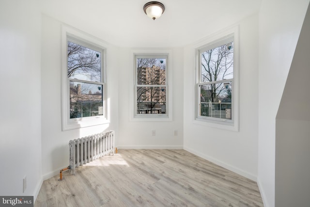 empty room featuring light hardwood / wood-style floors, radiator heating unit, and plenty of natural light